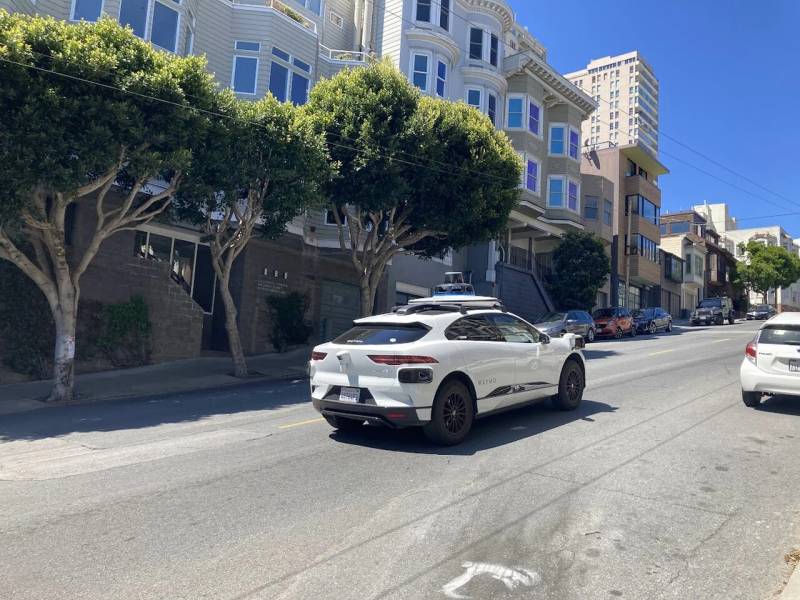Waymo autonomous vehicle operating on city streets in San Francisco utilizing roof-mounted LiDAR and computer vision sensors.