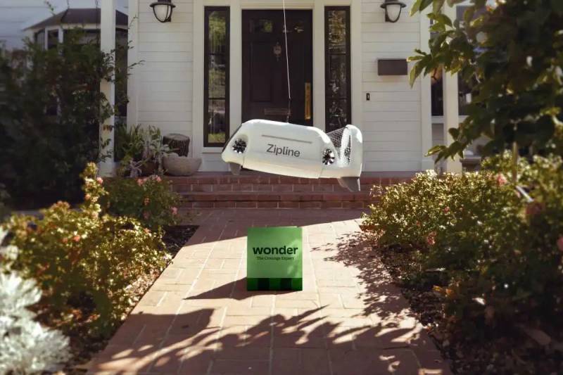 Zipline autonomous delivery drone cruising quietly through clear blue sky above suburban homes.